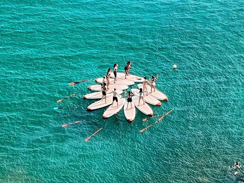 A group of participants practicing yoga on a stand-up paddleboard on the calm ocean waters with the scenic Falésia Cliffs in the background.